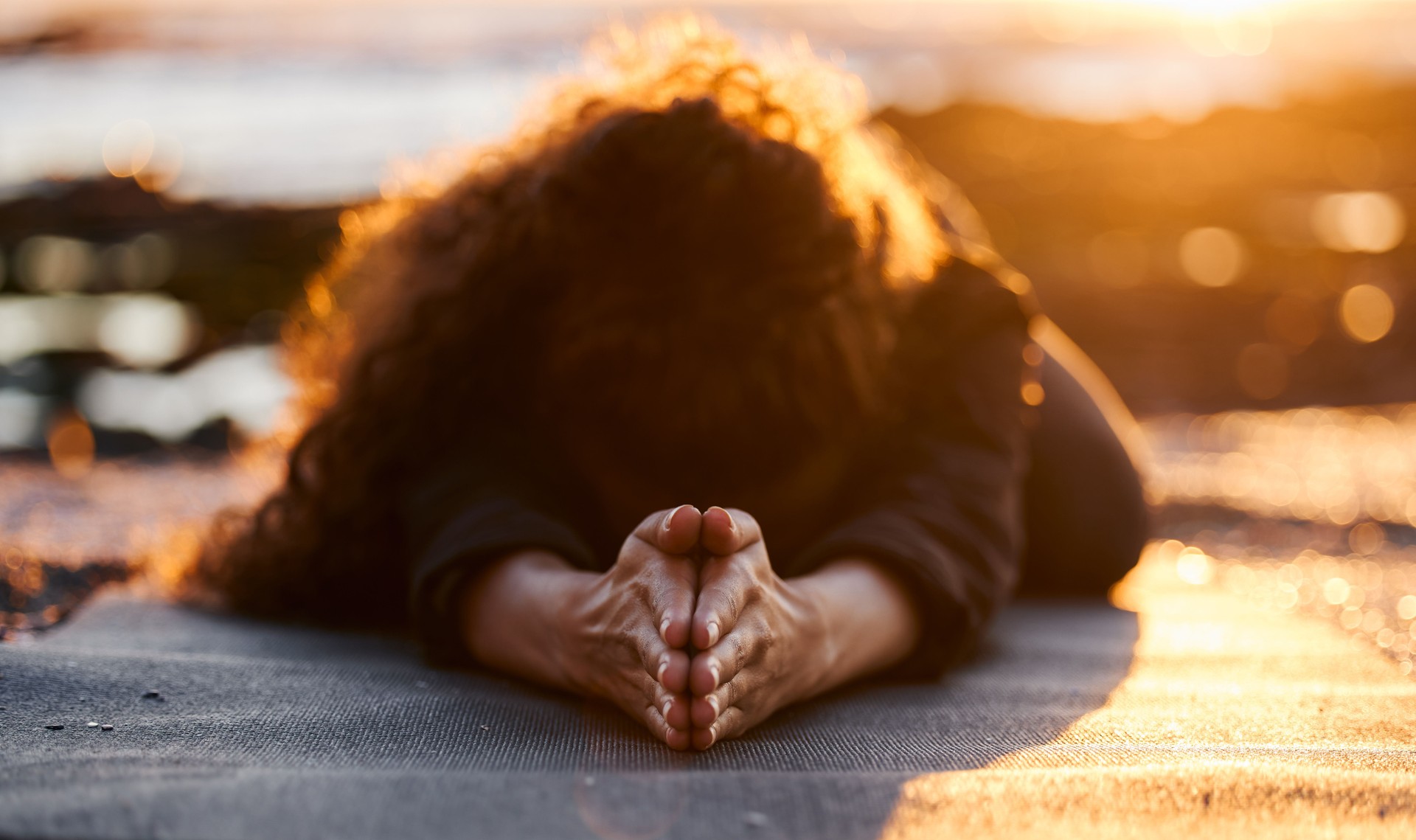 Shot of an unrecognizable woman doing yoga alone on the beach at sunset